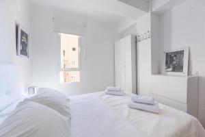 a white bedroom with two beds and two windows at AlmeriaSuite Las Caracolas Beach in Almería