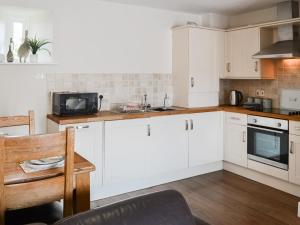 a kitchen with white cabinets and a table and a microwave at Heron Cottage in Alnham