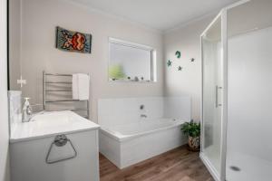 a white bathroom with a tub and a sink at Golden Dawn in Waihi Beach +10 photos