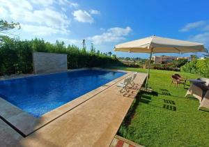a swimming pool with an umbrella and chairs at فيلا فاخرة أول صف على البحيرة الرملية in El Alamein