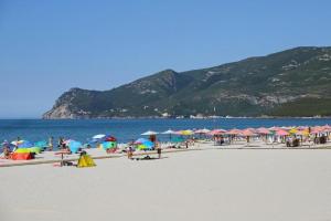 a group of people sitting on a beach with umbrellas at Alex Guest House in Quinta do Anjo