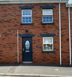 ein Backsteingebäude mit einer schwarzen Tür und zwei Fenstern in der Unterkunft The Grey Door 2 Bed Cottage Banbridge Parking Private Garden l WeStay Belfast Short Lets And Serviced Accommodations in Banbridge