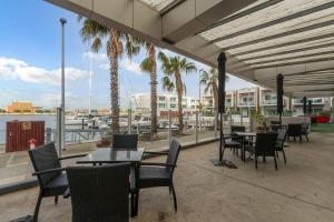 Un patio con mesas y sillas y palmeras. en Waterfront Stay with Marina Views and Easy CBD Access, en Glanville