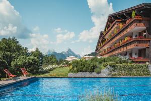 a resort with a swimming pool and mountains in the background at ERMITAGE Wellness- & Spa-Hotel in Gstaad
