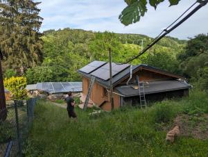 ArnoldshammerWichtelhaisl Rittersgrün im Erzgebirge - Entspannen im fröhlichen Tiny House - umzäunter Naturgarten-Hunde willkommen-Ebike und Elektroauto laden的一名男子站在一栋装有太阳能电池板的房子前