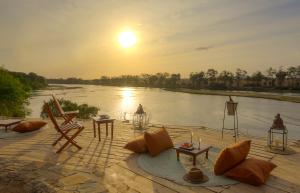 a sunset over a river with chairs and tables at Kudu Safari Camp in Koito