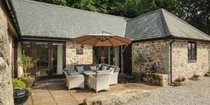 a patio with an umbrella and chairs and a table at Lydgate Cottage, Dartmoor in Postbridge