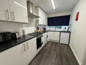 a kitchen with white cabinets and a black counter top at 4 Bed House - Free Parking - 8 min LGW Airport in Crawley