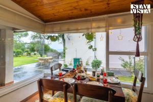 a dining room with a table and chairs and a large window at StayVista at Ellis Ville with Bonfire, Lawn in Kasauli