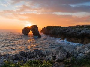 a rock in the ocean with the sun setting at Apartamento La Vega de Santiago 2 in Posada de Llanes +18 photos