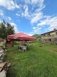 a group of tables and chairs under a red umbrella at Chvibiani Guesthouse & Bar in Ushguli