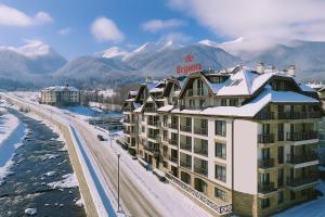 a hotel in the snow with mountains in the background at Regnum Bansko Ski Hotel & SPA in Bansko