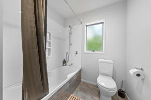 a white bathroom with a toilet and a bath tub at Birdsong Retreat - Titirangi Holiday Home in Auckland +13 photos
