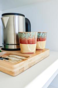 two cups on a cutting board next to a coffee pot at Hotel du Balcon in Capbreton