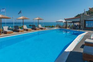 a swimming pool with chairs and umbrellas next to the ocean at Violetta Seaside Studios&Apartments in Karlovasi
