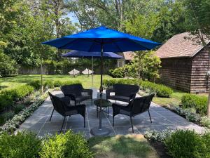 a patio with chairs and a table with a blue umbrella at Wainscott Woods Retreat in Wainscott