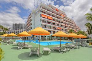 Una piscina con sillas y sombrillas frente a un edificio. en Sunset Tenerife, en Playa de las Américas