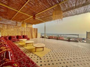 a living room with a couch and tables and the ocean at SurfsHub Hostel Tghazout Bay Tamraght in Tamraght Ouzdar