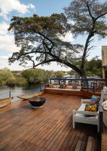 a wooden deck with chairs and a tree and water at Zambezi Dusk in Livingstone