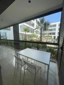 a white table and chairs in a room with a large window at Appartement Luxe Vue Piscine Résidence Les Perles de Bentriaa, El Mansouria in Mohammedia