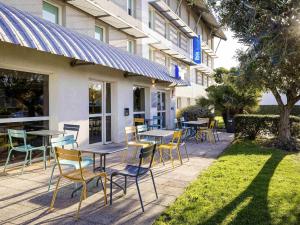 Un patio con mesas y sillas frente a un edificio. en ibis budget Carcassonne Aéroport - A61, en Carcassonne