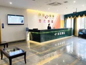 a man standing at a counter in a waiting room at Shell Hotel Luzhou Longmatan District Dujia Street Riverside in Luzhou