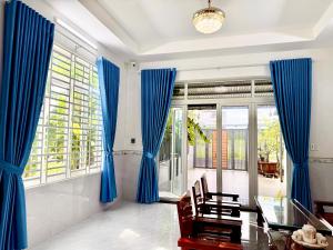 a dining room with blue curtains and a glass table at Villa 1985 in Buon Ma Thuot