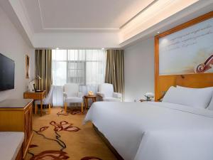 ein Hotelzimmer mit einem großen weißen Bett und einem Schreibtisch in der Unterkunft Vienna Hotel Hunan Shaoyang South Railway Station in Shaoyang