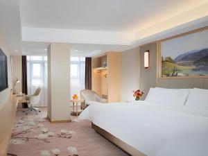 une chambre avec un grand lit blanc et un bureau dans l'établissement Vienna Hotel Guangxi Tiandong Times Plaza, à T'ien-tung