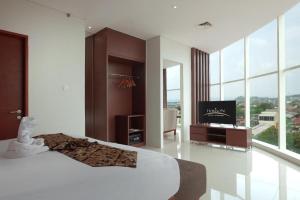 a bedroom with a bed and a tv and windows at Horison Nindya Semarang in Semarang