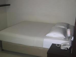 a bed with white sheets and pillows next to a table at Permata Hotel in Purwakarta
