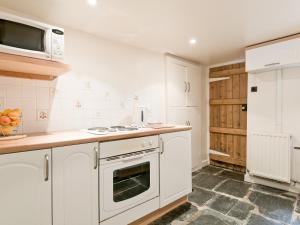 a white kitchen with a stove and a microwave at Rowlandson Ground Cottage in High Yewdale
