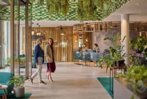 two people walking through a restaurant with plants at Hyatt Regency Amsterdam in Amsterdam