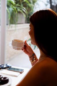 a woman sitting at a table drinking a cup of coffee at Hotel Puerta del Mar - Adults Recommended in Nerja