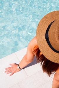 a woman wearing a straw hat sitting next to a swimming pool at Hotel Puerta del Mar - Adults Recommended in Nerja