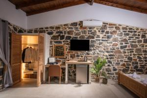 a room with a stone wall with a desk and a tv at Balsamico Traditional Suites in Hersonissos