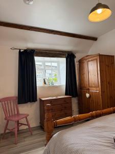 a bedroom with a bed and a chair and a window at Titmouse at Trenale Court Cottages in Tintagel