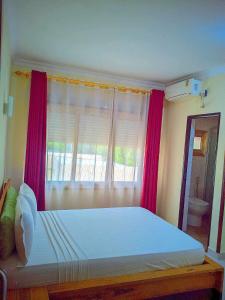 een slaapkamer met een bed met rode gordijnen en een raam bij New Park Resort in Mahajanga