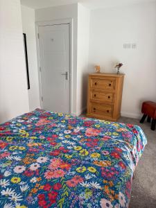 a bedroom with a bed with a floral bedspread and a dresser at The Nineteenth at Portstewart in Portstewart