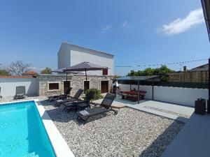 a swimming pool with chairs and umbrellas next to a house at Holiday Home Latin in Peruški