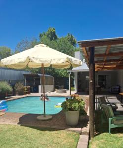 una piscina con ombrellone e tavolo e sedie di Aan de Granaat Gastehuis a Beaufort West