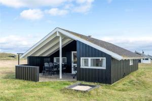 a black house in a field with a table and chairs at 150-Ringkobing-Krogen-8 in Ringkøbing