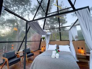 ein Schlafzimmer in einem Glashaus mit einem Bett und zwei Stühlen in der Unterkunft Villa das Cabanas – Viva o Luxo da Natureza em Piri in Pirenópolis