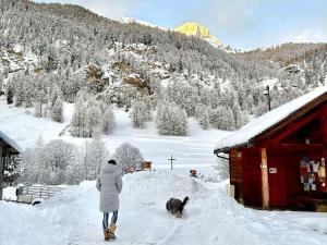 una persona che porta a spasso il cane nella neve accanto a una baita di CASA-La Lorraine lovely studio in a chalet St-Véran 4p a La Chalp-Sainte-Agathe