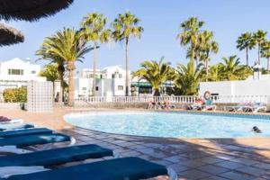 a swimming pool with blue lounge chairs and palm trees at Casa Roma in Puerto del Carmen