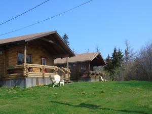 a log cabin with two chairs in front of it at Cajun Cedar Log Cottages Ltd in Margaree Forks