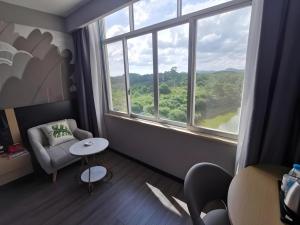 Cette chambre comprend une chaise, une table et une grande fenêtre. dans l'établissement Thank Inn Hotel Guangxi Qinzhou Lingshan Renhe, à Lingshan