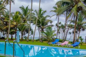 a resort swimming pool with palm trees and chairs at Zapo Villa in Balapitiya