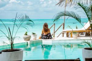 a woman sitting next to a swimming pool overlooking the ocean at Pili Pili Tropical Island in Jambiani