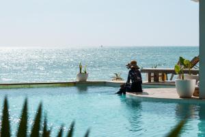a woman sitting next to a swimming pool overlooking the ocean at Pili Pili Tropical Island in Jambiani